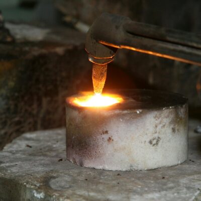 A close-up view of a metal smelting process using a torch, illustrating heat and sparks.