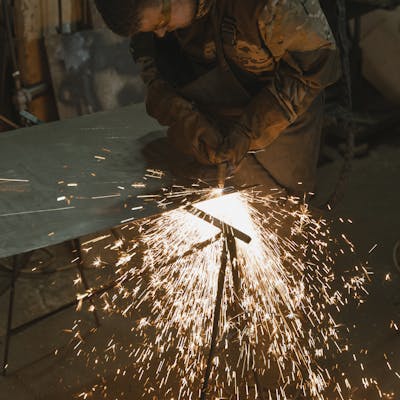 A professional welder cutting metal in an industrial workshop with bright sparks flying around.