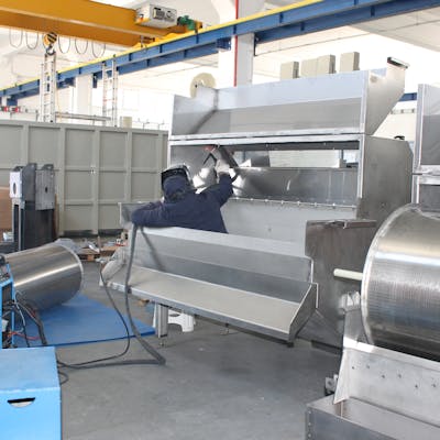 A worker welds metal machinery inside an industrial facility, showcasing production processes.
