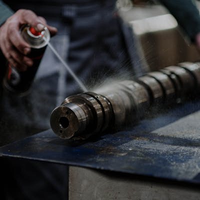 Mechanic meticulously sprays degreaser onto an engine camshaft for maintenance.