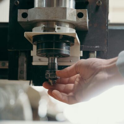 Detailed shot of a CNC machine spindle being adjusted by a human hand in a workshop setting.